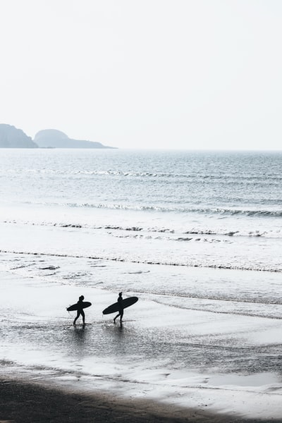 两个人白天在海滩上玩冲浪板